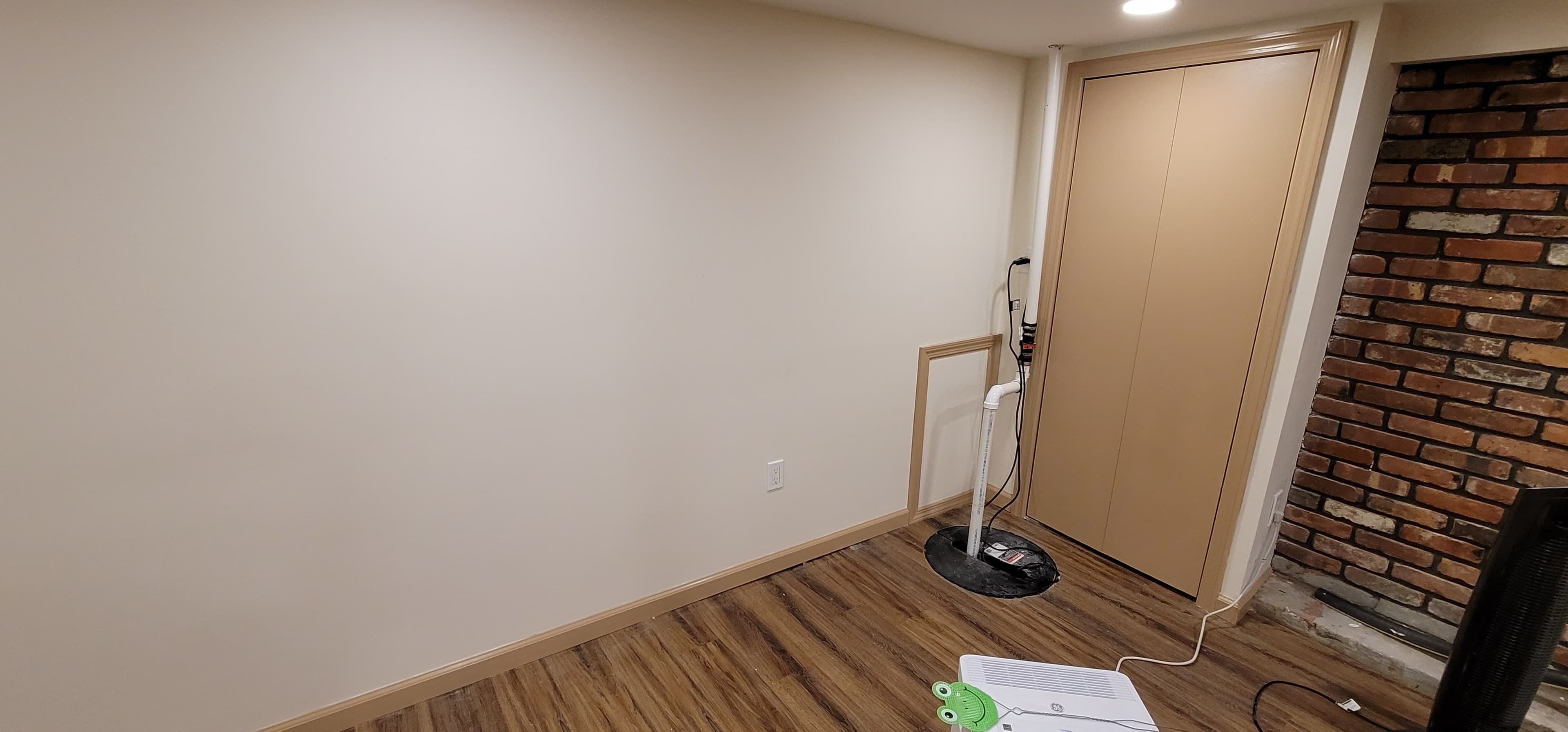 Finished basement with cream walls, dark LVP flooring, utility closet, and brick accent wall, Rockland County NY