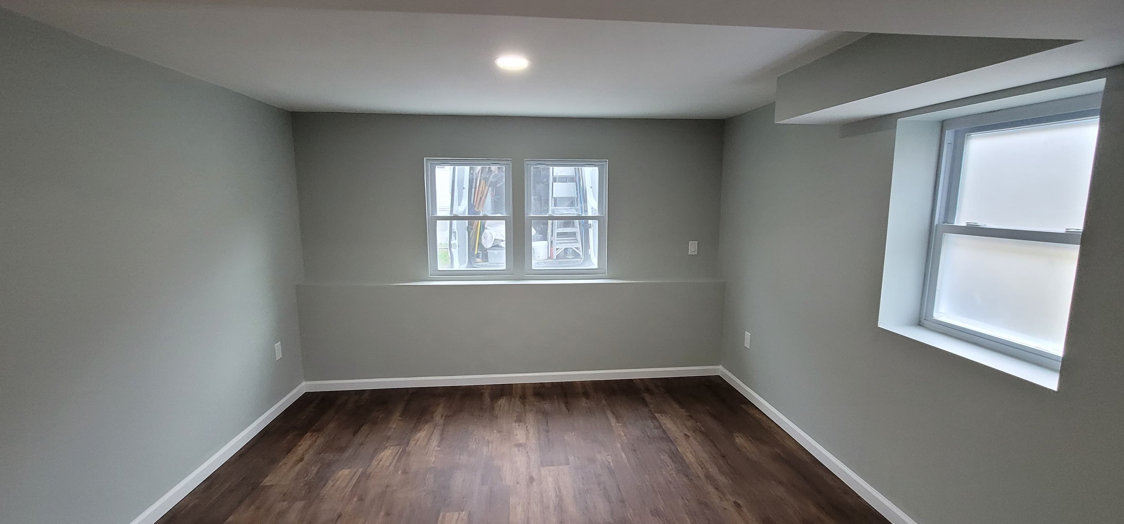 Finished basement room with gray walls, dark LVP flooring, and double egress windows, Rockland County NY