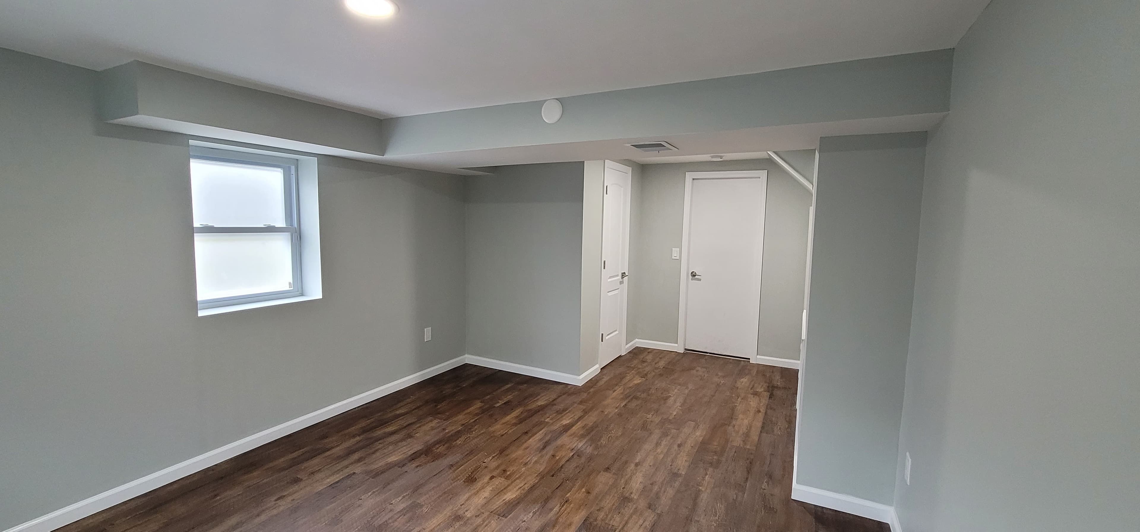 Finished basement with dark LVP flooring, gray walls, and windows in Rockland County NY by Q's Home Improvement