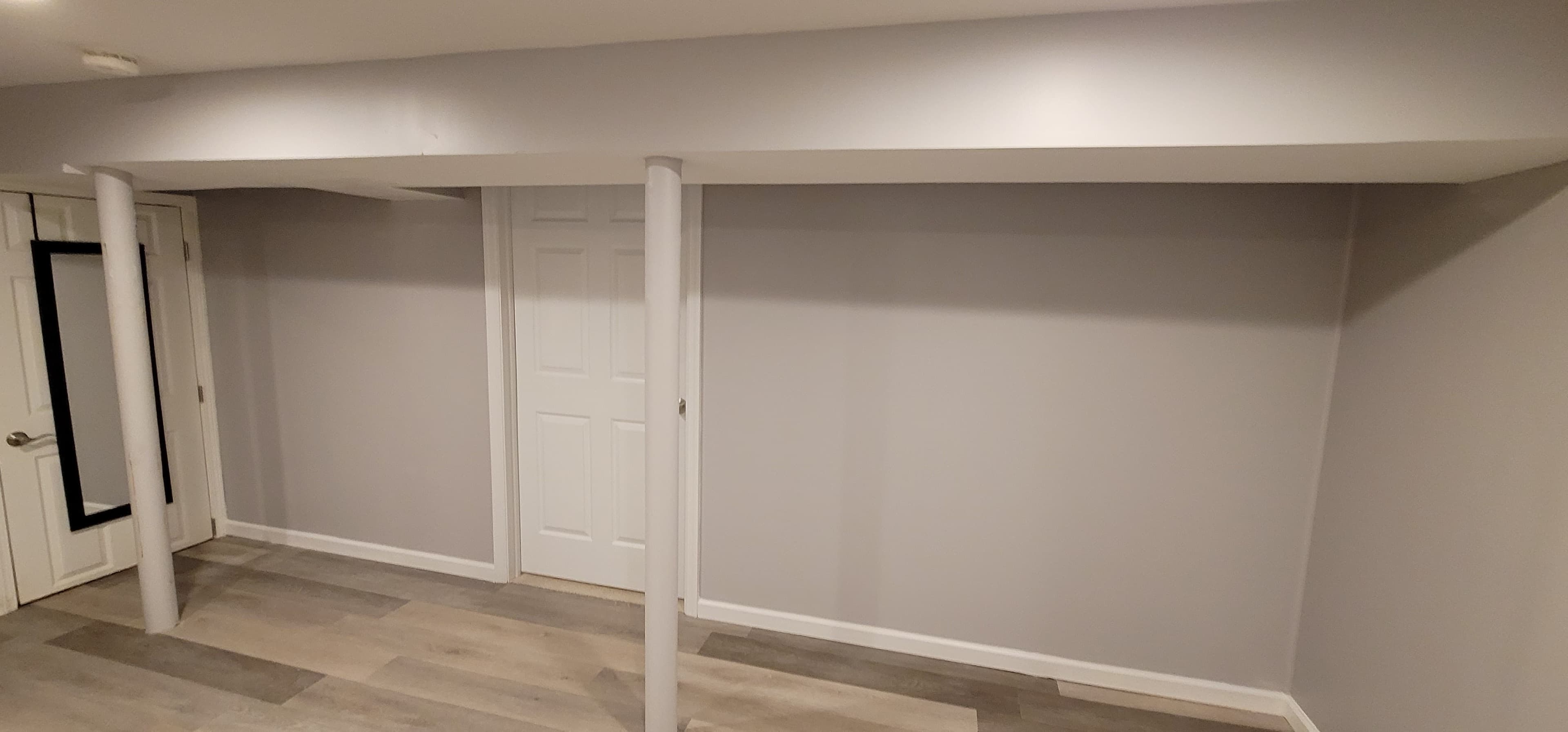 Finished basement with gray walls, light LVP flooring, wrapped column, and white doors, Rockland County NY
