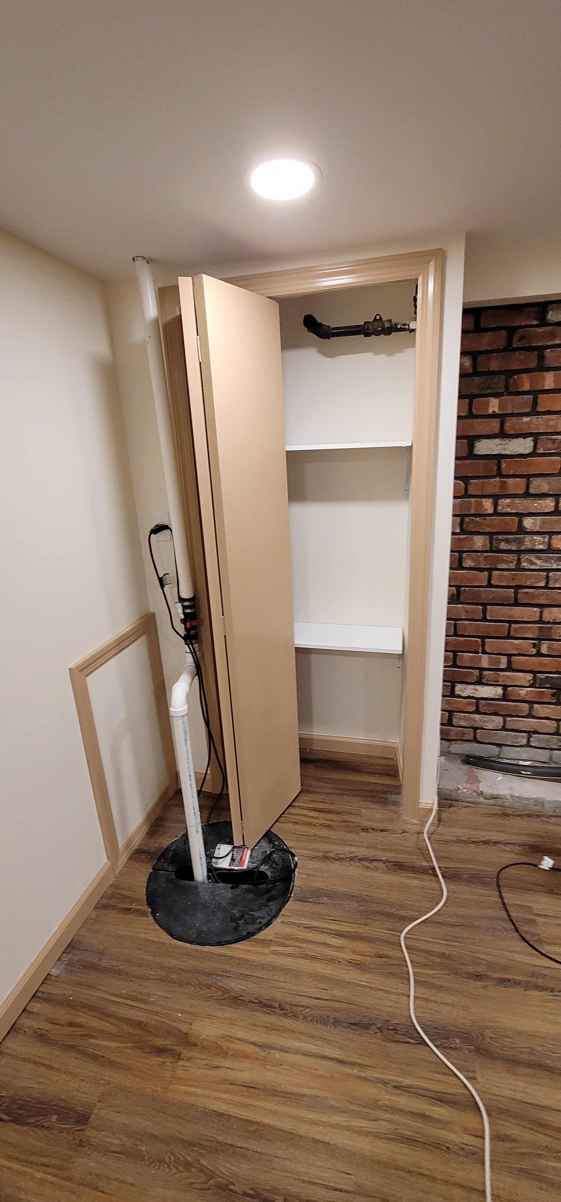 Finished basement utility closet with shelving, sump pump enclosure, brick accent, and LVP flooring, Rockland County NY