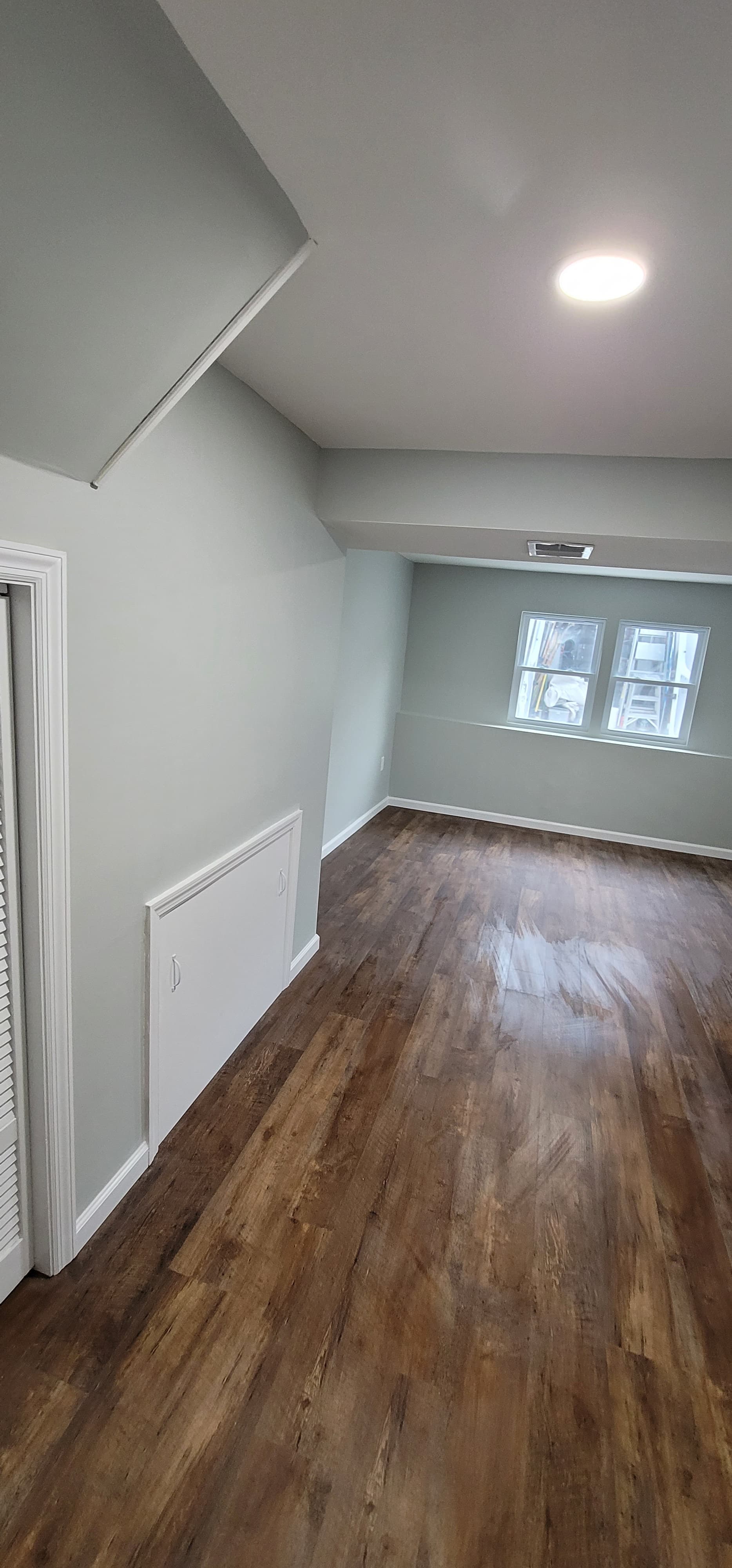 Finished basement with vaulted ceiling, blue-gray walls, dark LVP flooring, and egress window, Rockland County NY