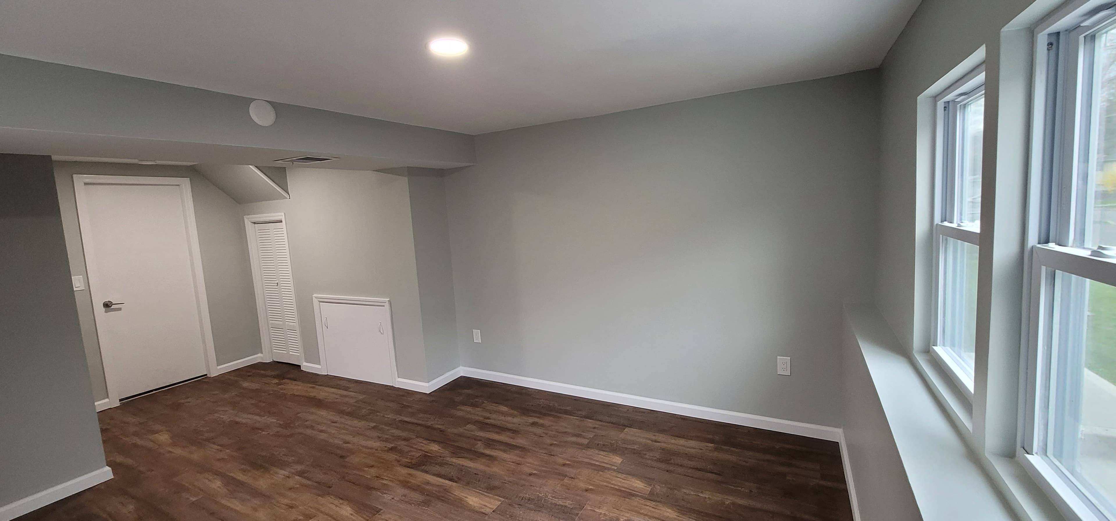 Finished basement wide view — gray-blue walls, dark LVP flooring, windows, and doors, Rockland County NY