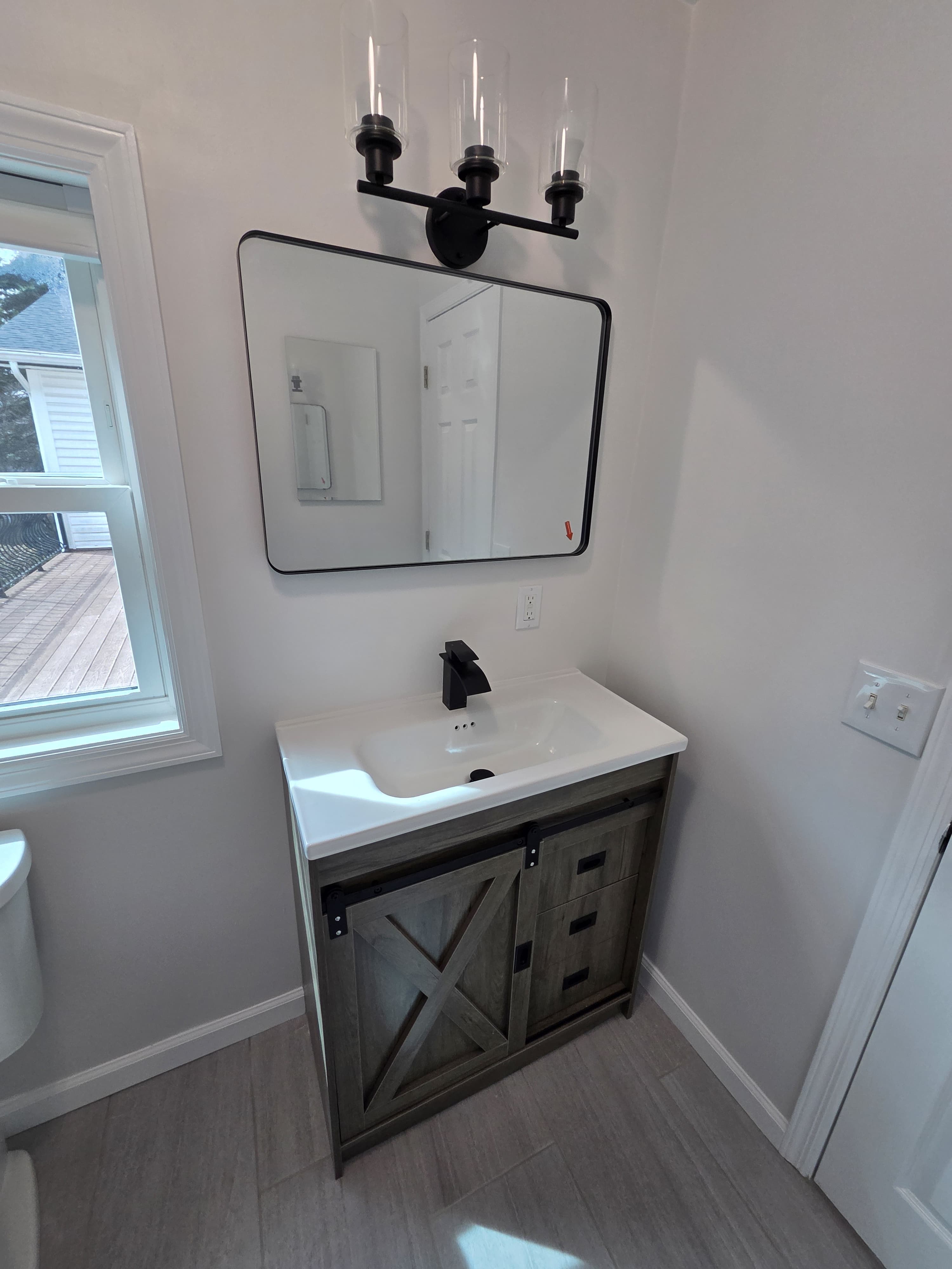 Bathroom vanity with gray barn-door cabinet, black faucet, black frame mirror, and black light fixture, Rockland County NY