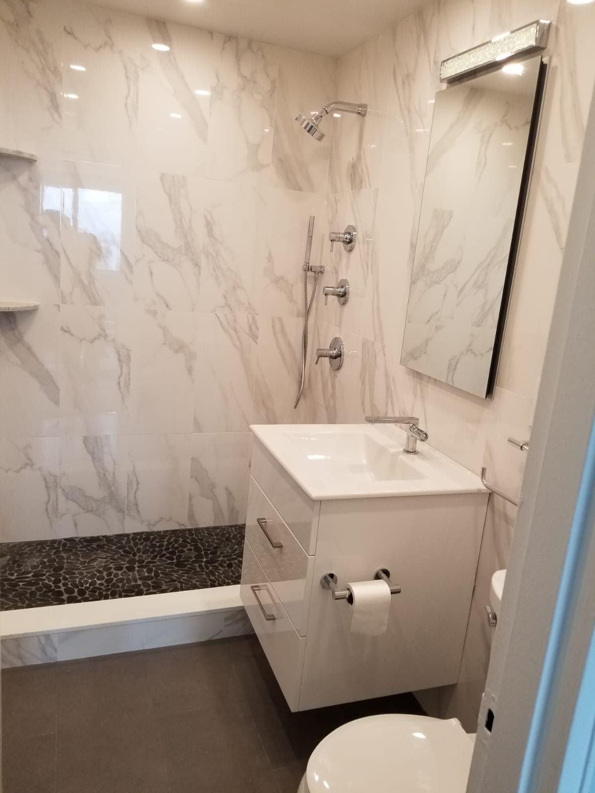Walk-in shower with Carrara marble-look tile, chrome multi-function shower system, and pebble floor, Rockland County NY