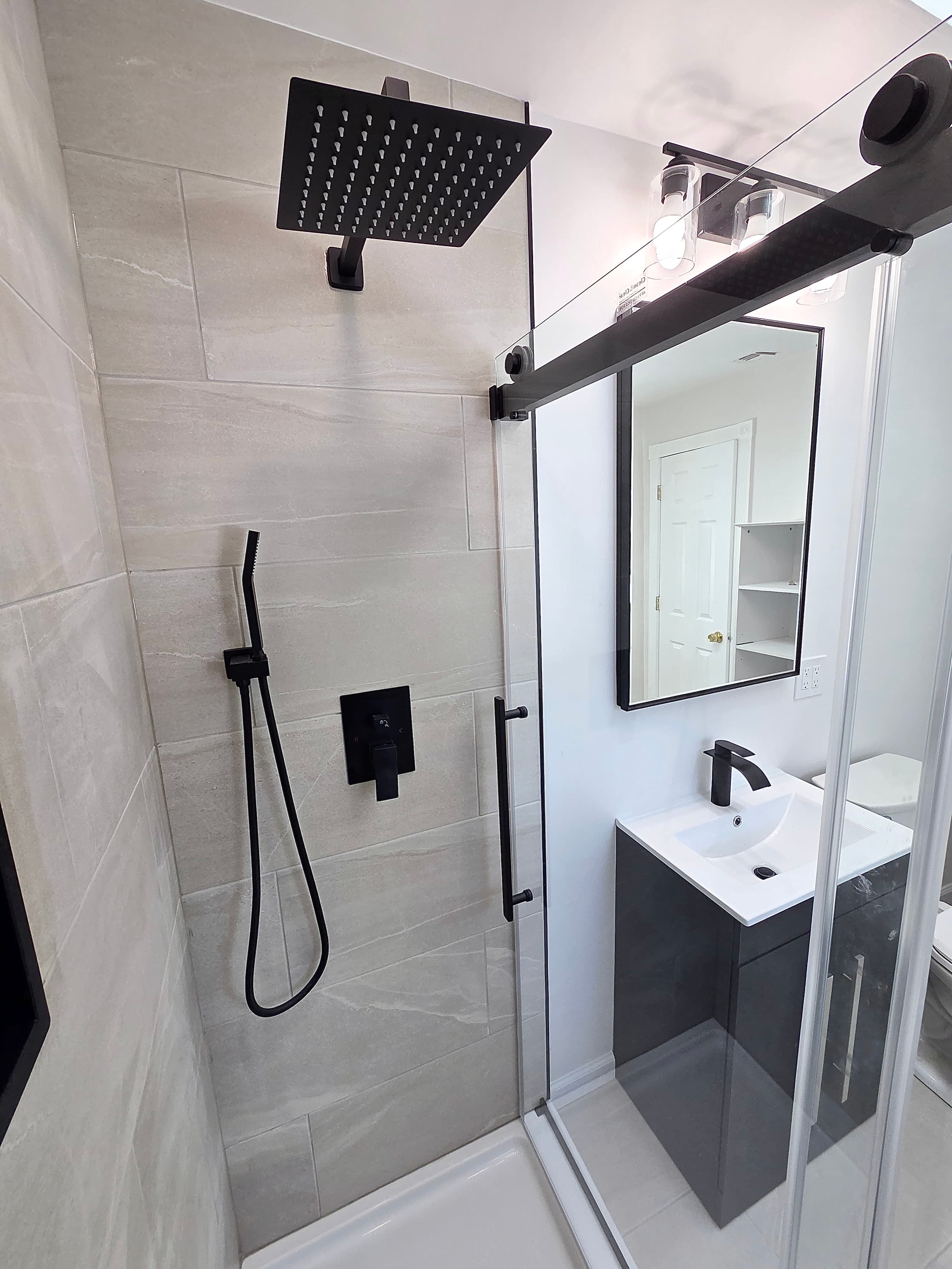 Compact bathroom remodel with large format gray tile shower, black rain head, and small dark vanity, Rockland County NY