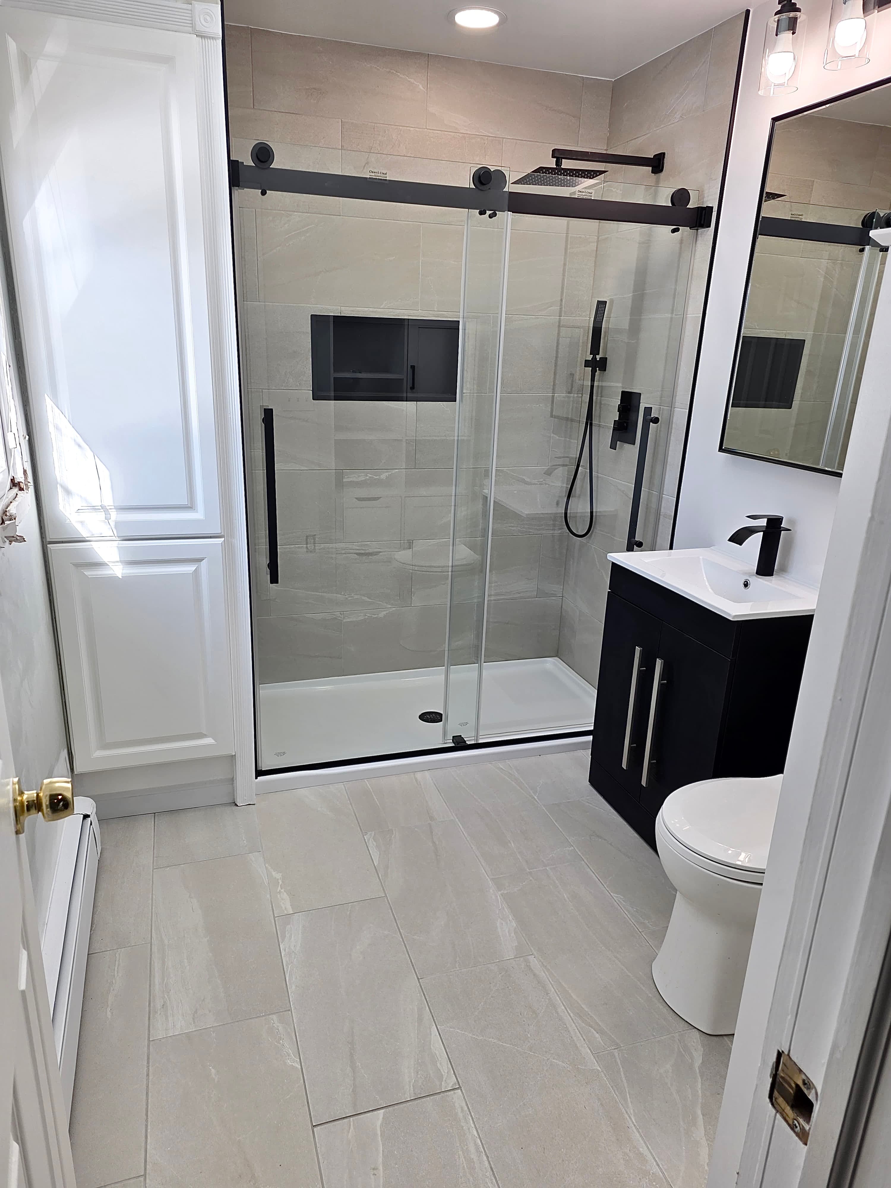 Full bathroom remodel with gray large format tile, black sliding barn door shower, and dark floating vanity, Rockland County NY