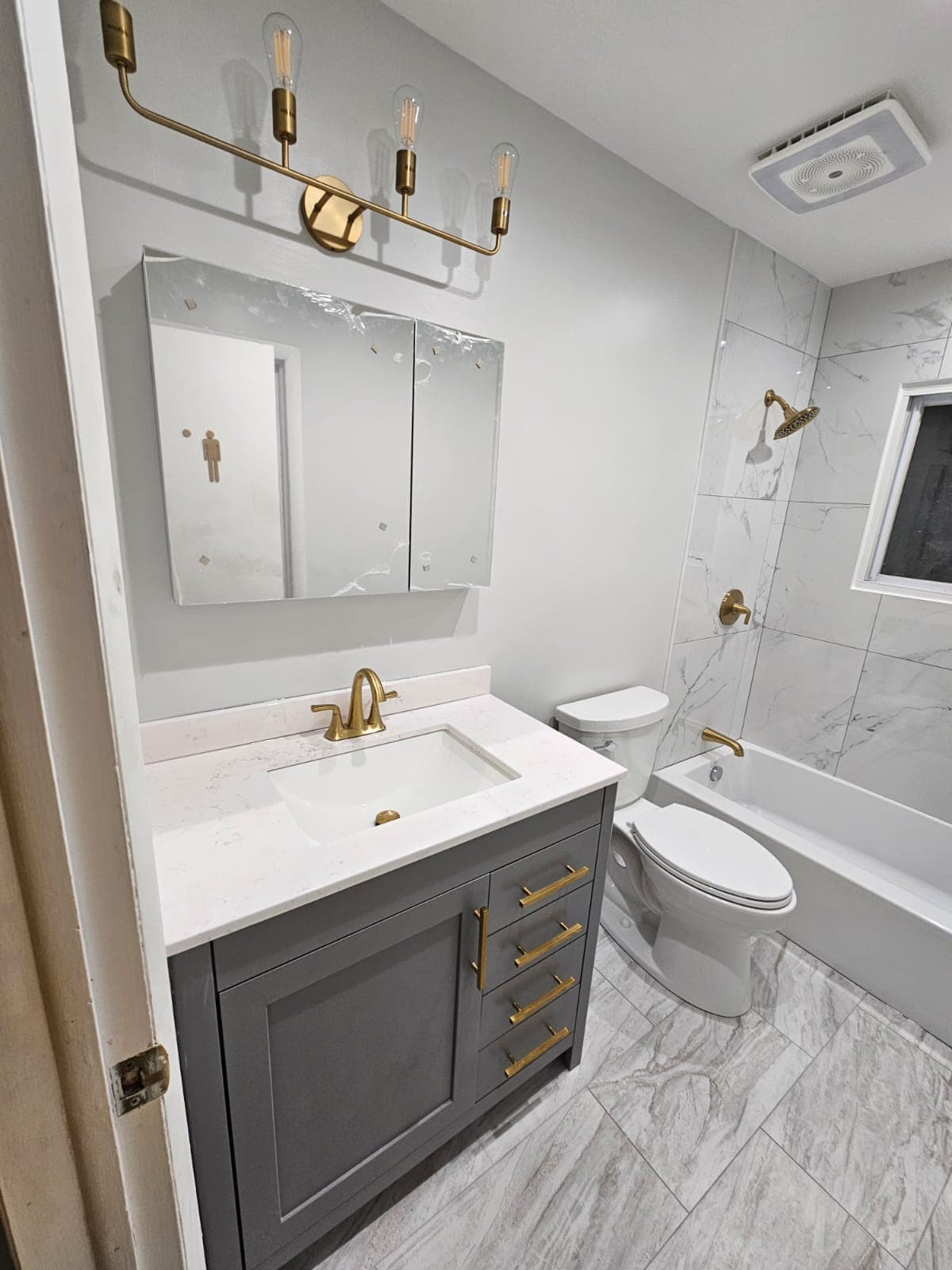 Bathroom remodel with gray vanity, gold hardware, brass faucet, and marble-look tile tub surround, Rockland County NY