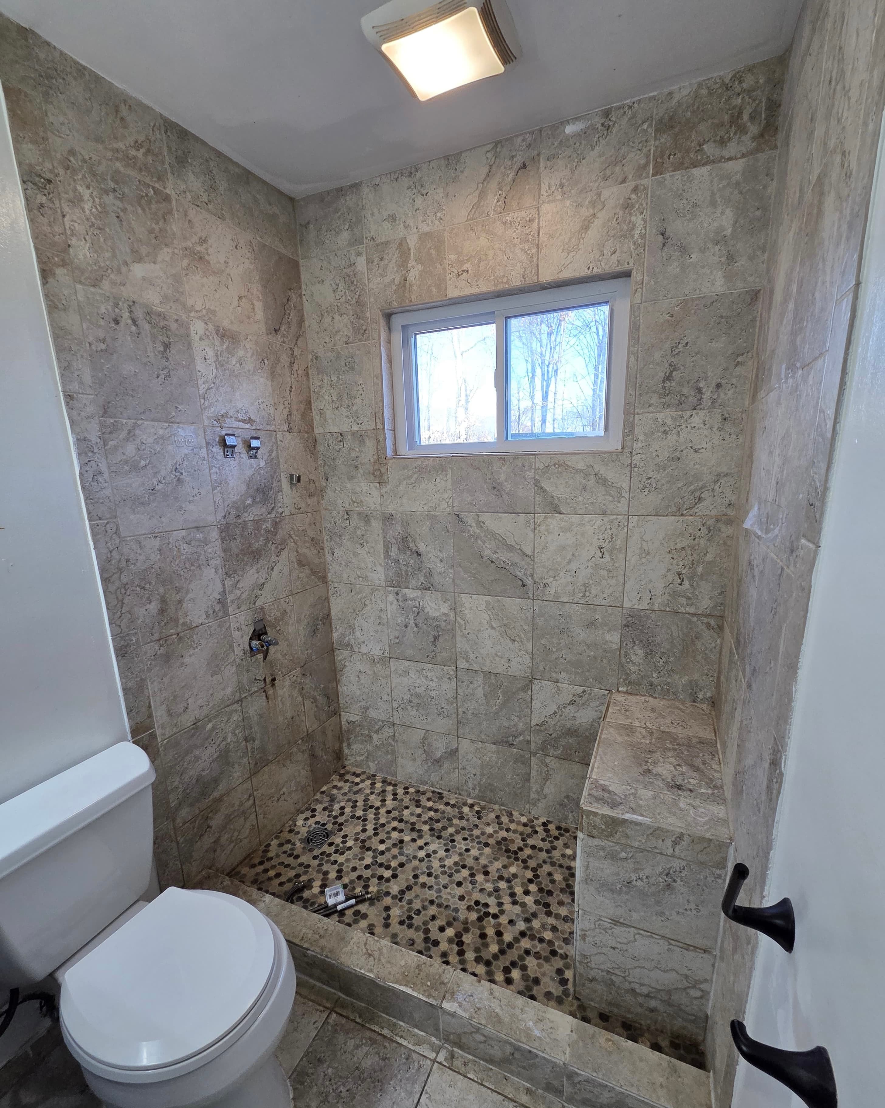 Walk-in shower with travertine stone tile, built-in bench, and penny mosaic floor, Rockland County NY